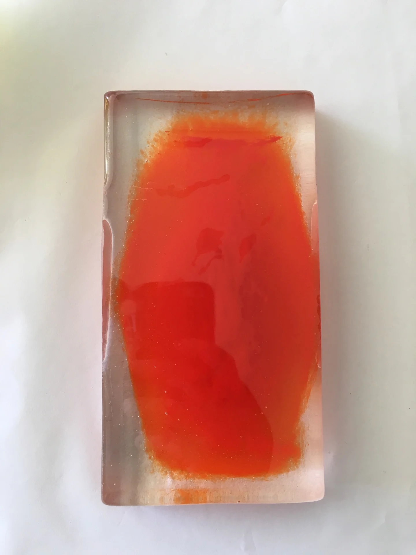 A translucent-looking rectangular form has a large irregular red-orange field at its centre against a pale background.