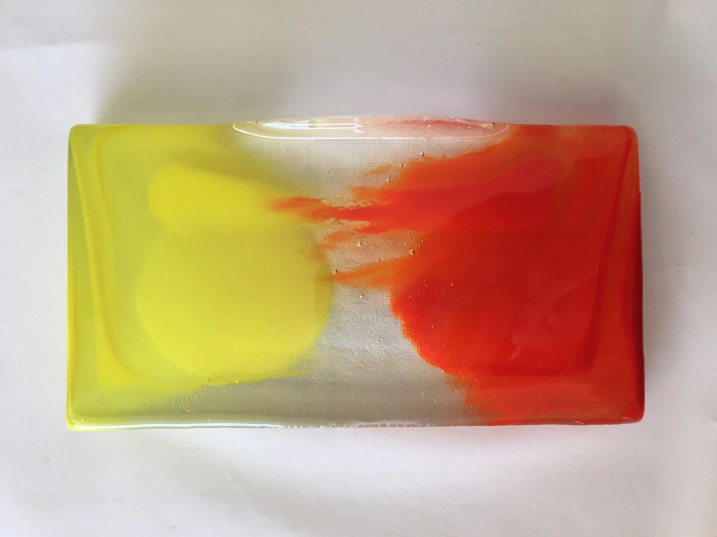 A horizontal rectangular form on a pale background holds a yellow field at left and a red-orange field at right, with soft pale colour between them.