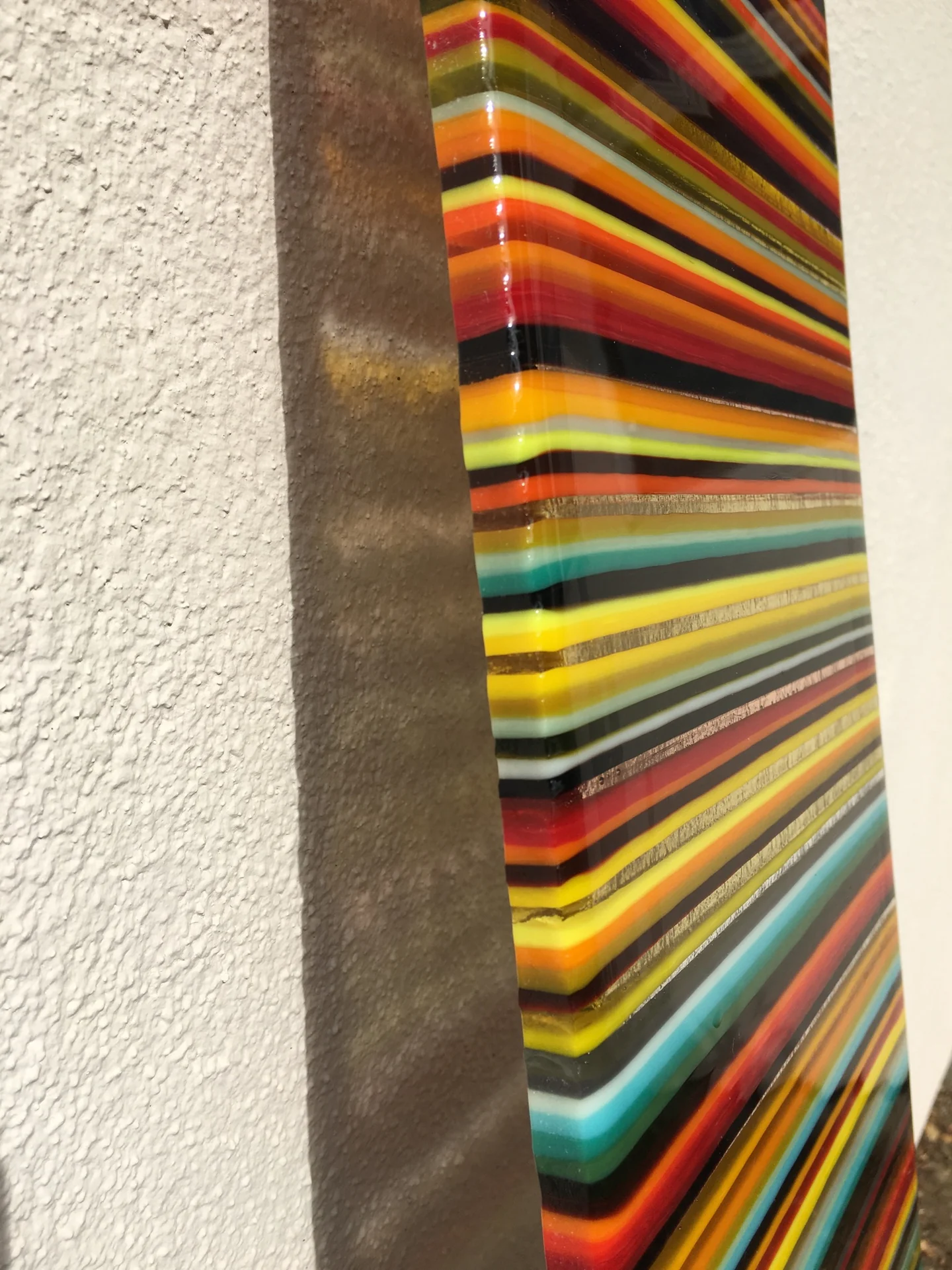 A close side view shows yellow, orange, green and blue bands beside a broad dark edge against a pale wall.