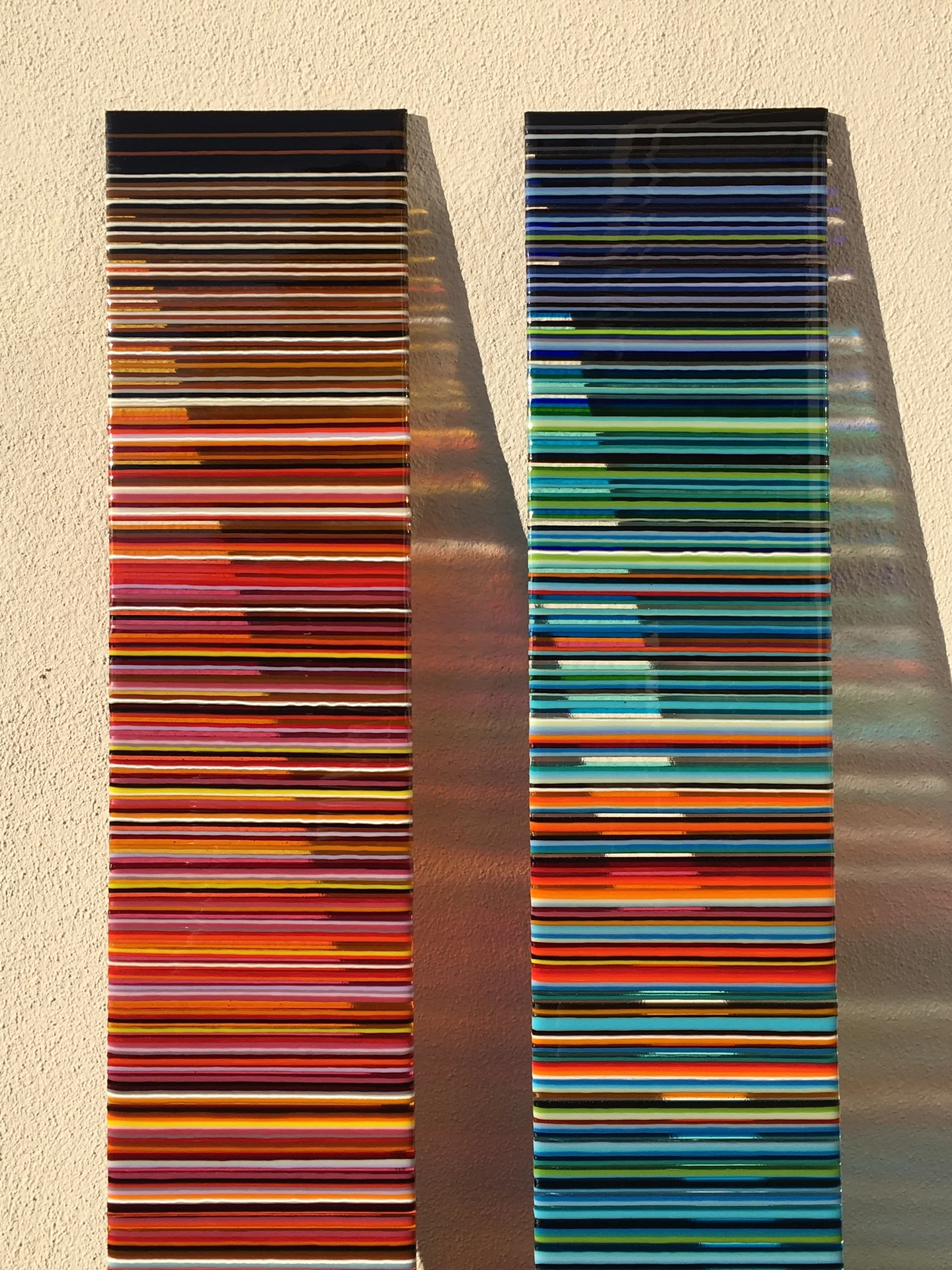 Two tall striped panels stand side by side against a pale wall, one mostly red and orange and the other mostly blue and turquoise.