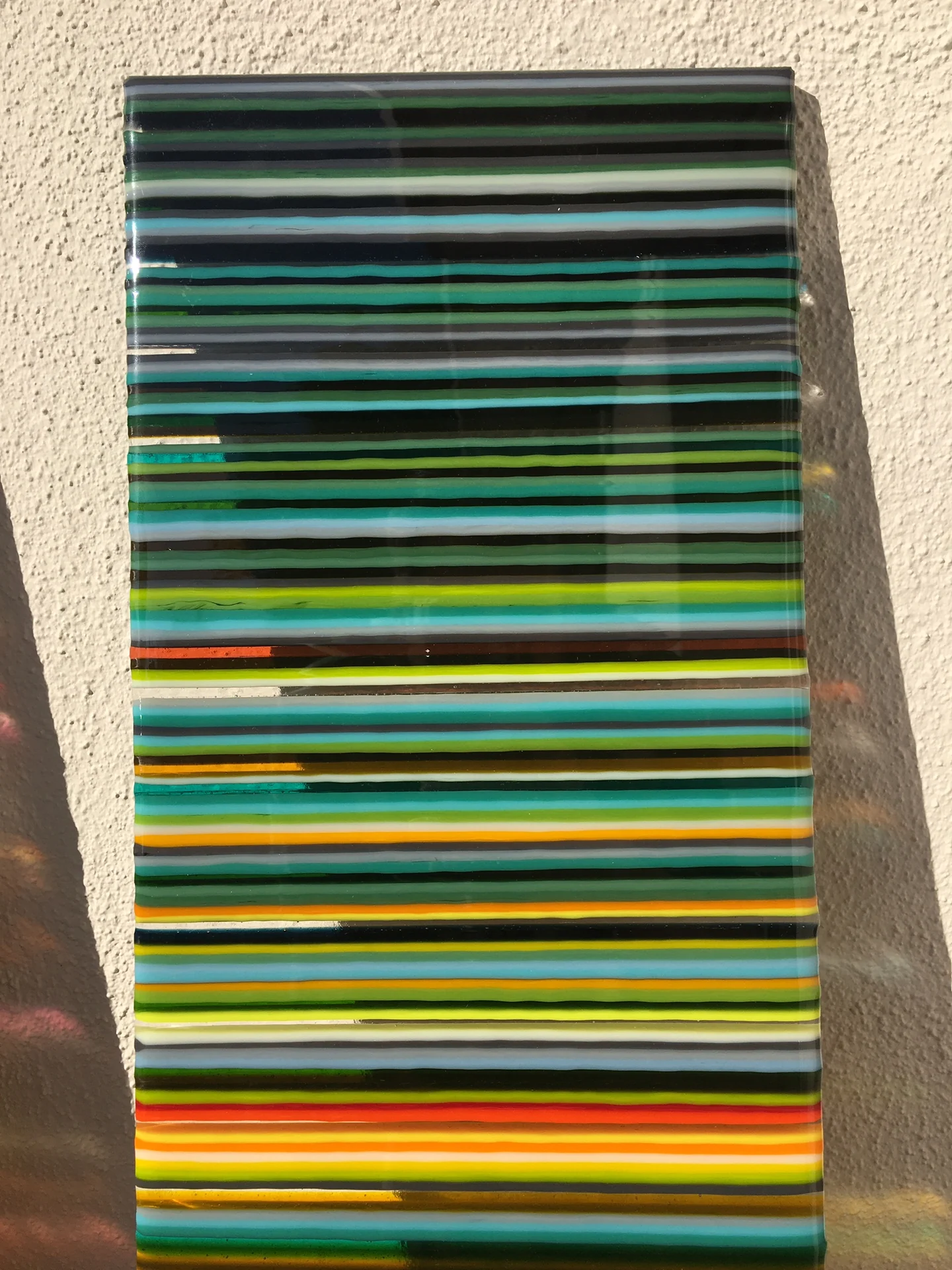 A front-facing tall panel is filled with thin blue, turquoise and green horizontal stripes, with yellow bands near the bottom.
