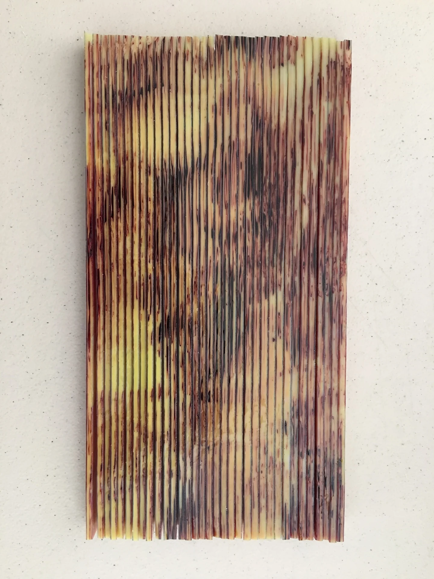 A vertical rectangular composition against a pale background has closely spaced dark lines over mottled cream, yellow, brown and muted pink areas.