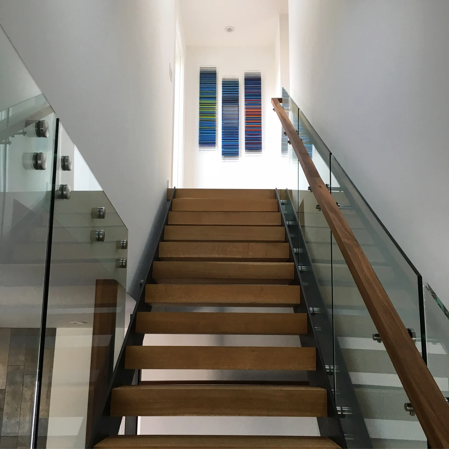 Three narrow, horizontally striped glass panels seen beyond a wooden stair with glass balustrades