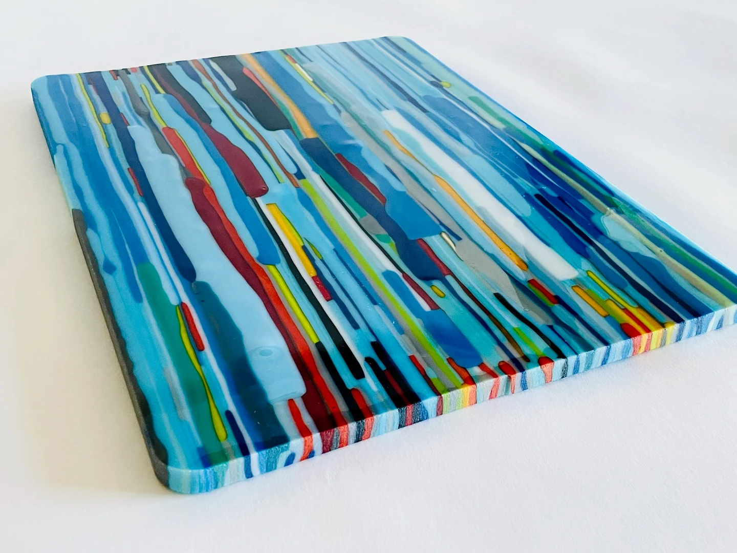 Angled close view of a blue-dominant glass panel with narrow red, yellow, green, white and dark bands and a striped edge