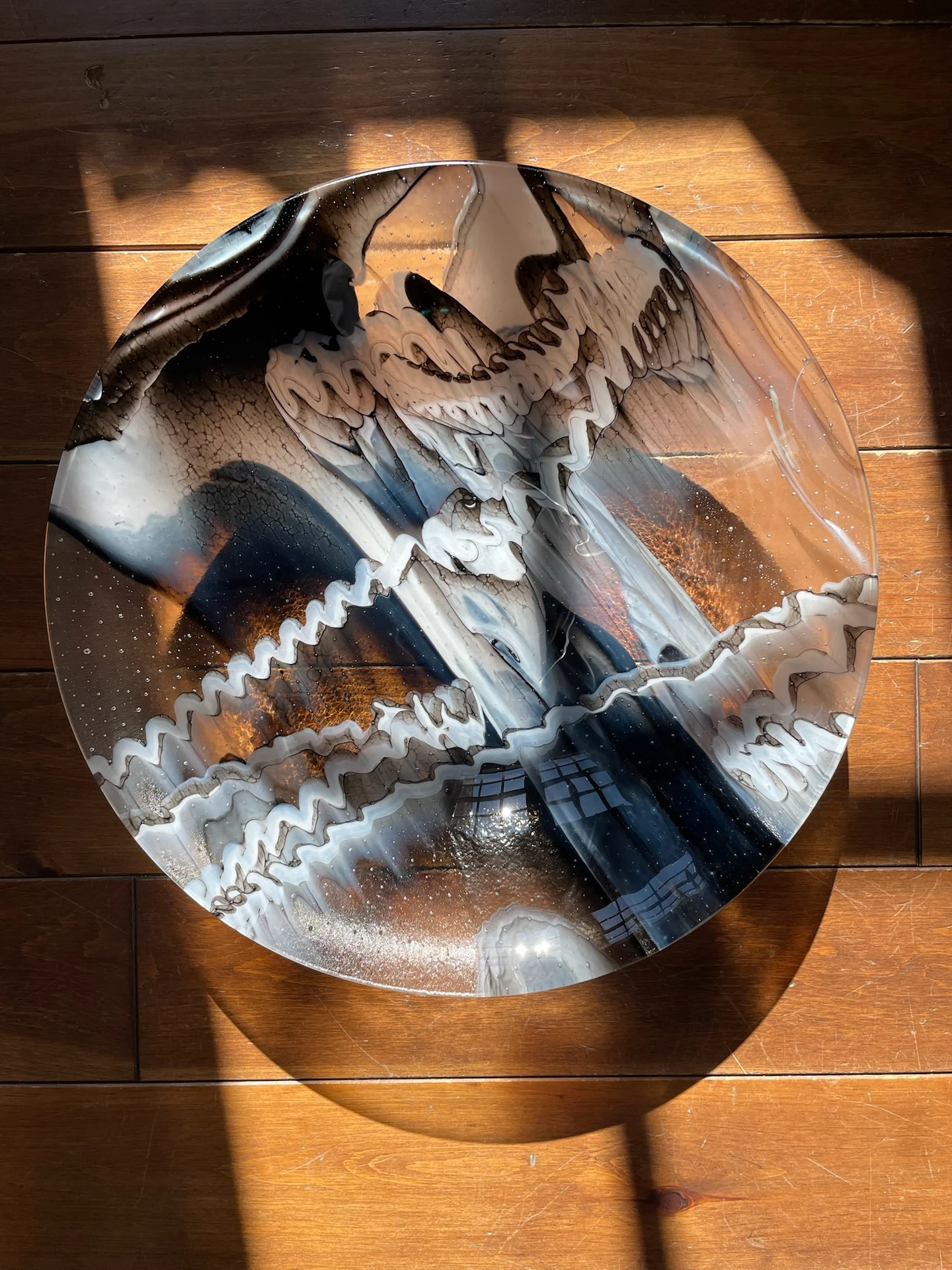 Round bowl with black, white and grey flowing patterns seen from above on a wooden floor
