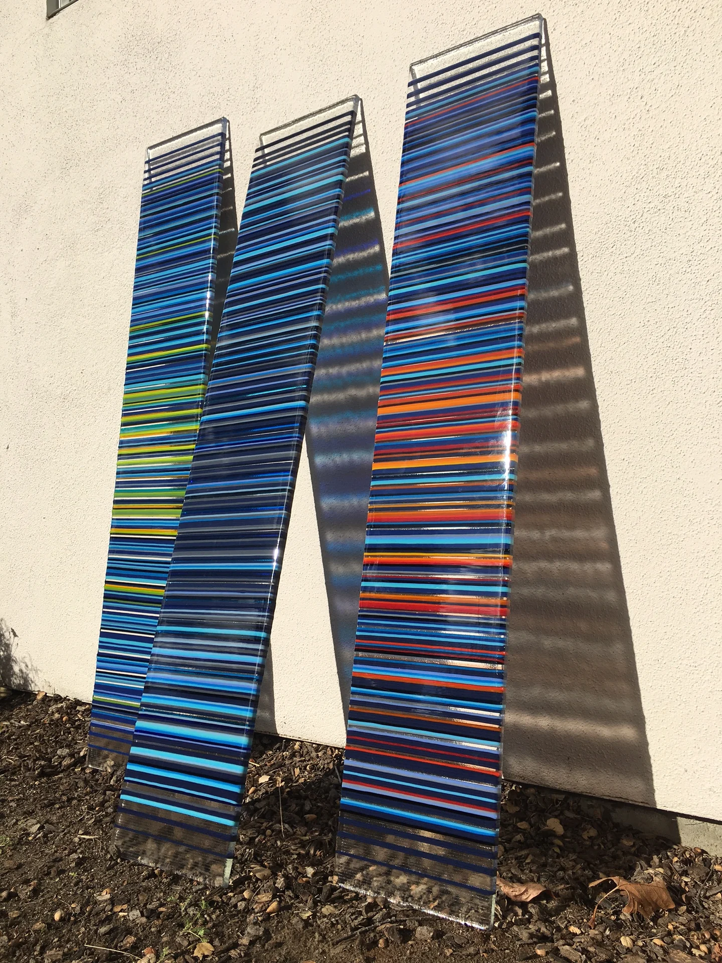 Three blue-striped panels leaning outdoors against a pale wall in sunlight