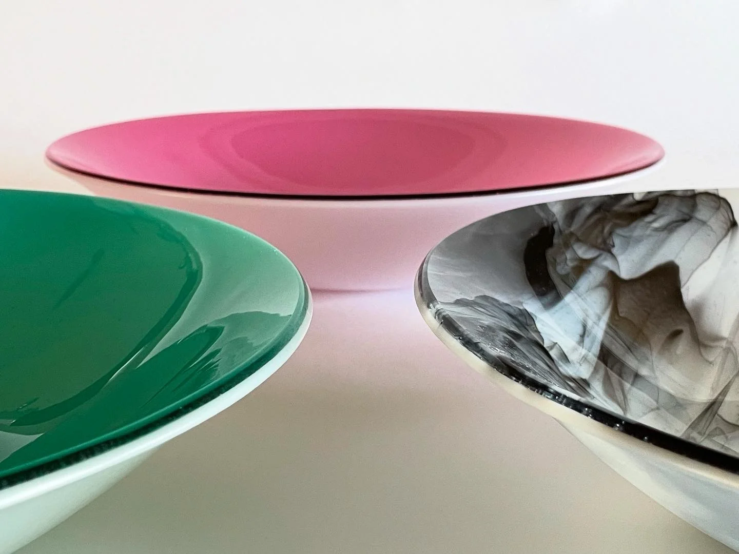 Three shallow circular forms in pink, green and black-and-white overlap against a pale background.