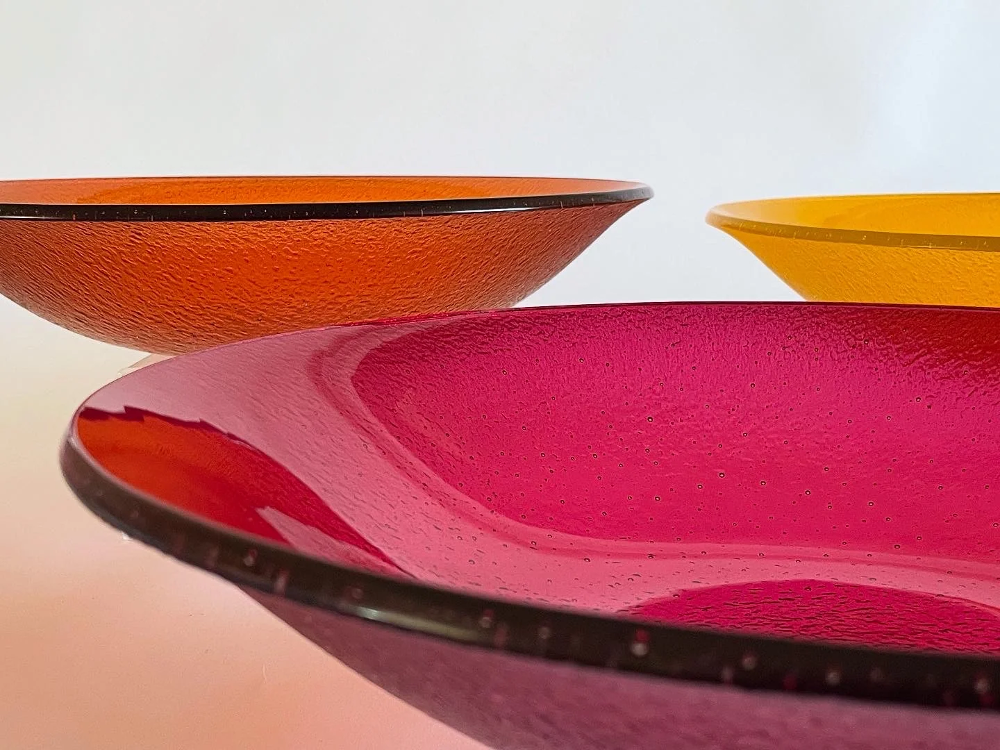 A vivid pink shallow form fills the foreground, with orange and yellow shallow forms behind it against white.