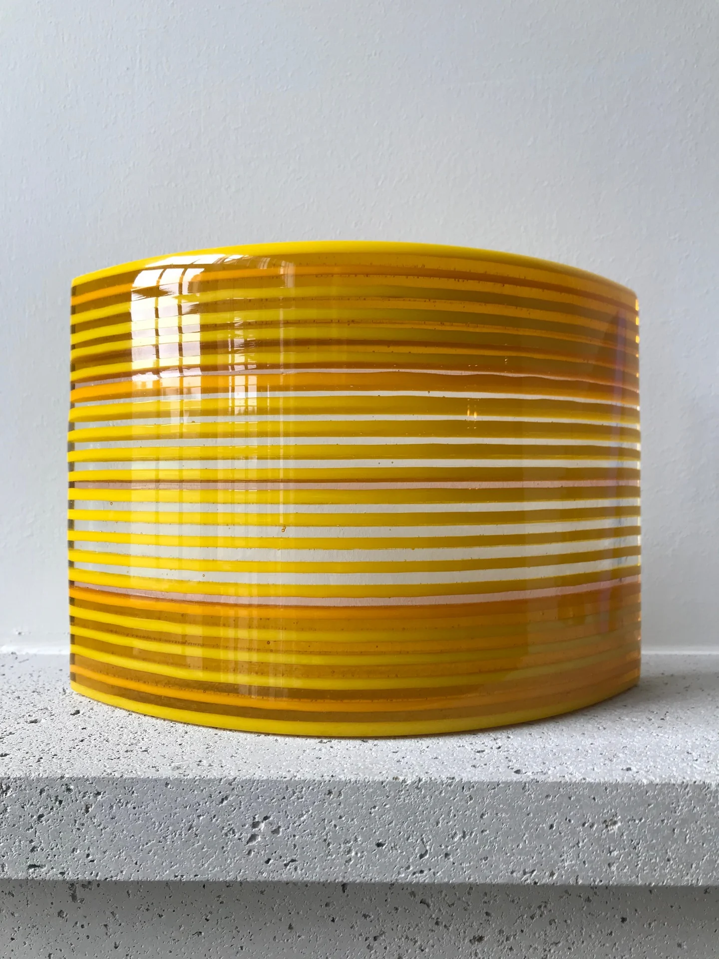 An upright curved form with closely spaced yellow and white horizontal bands stands on a light ledge.
