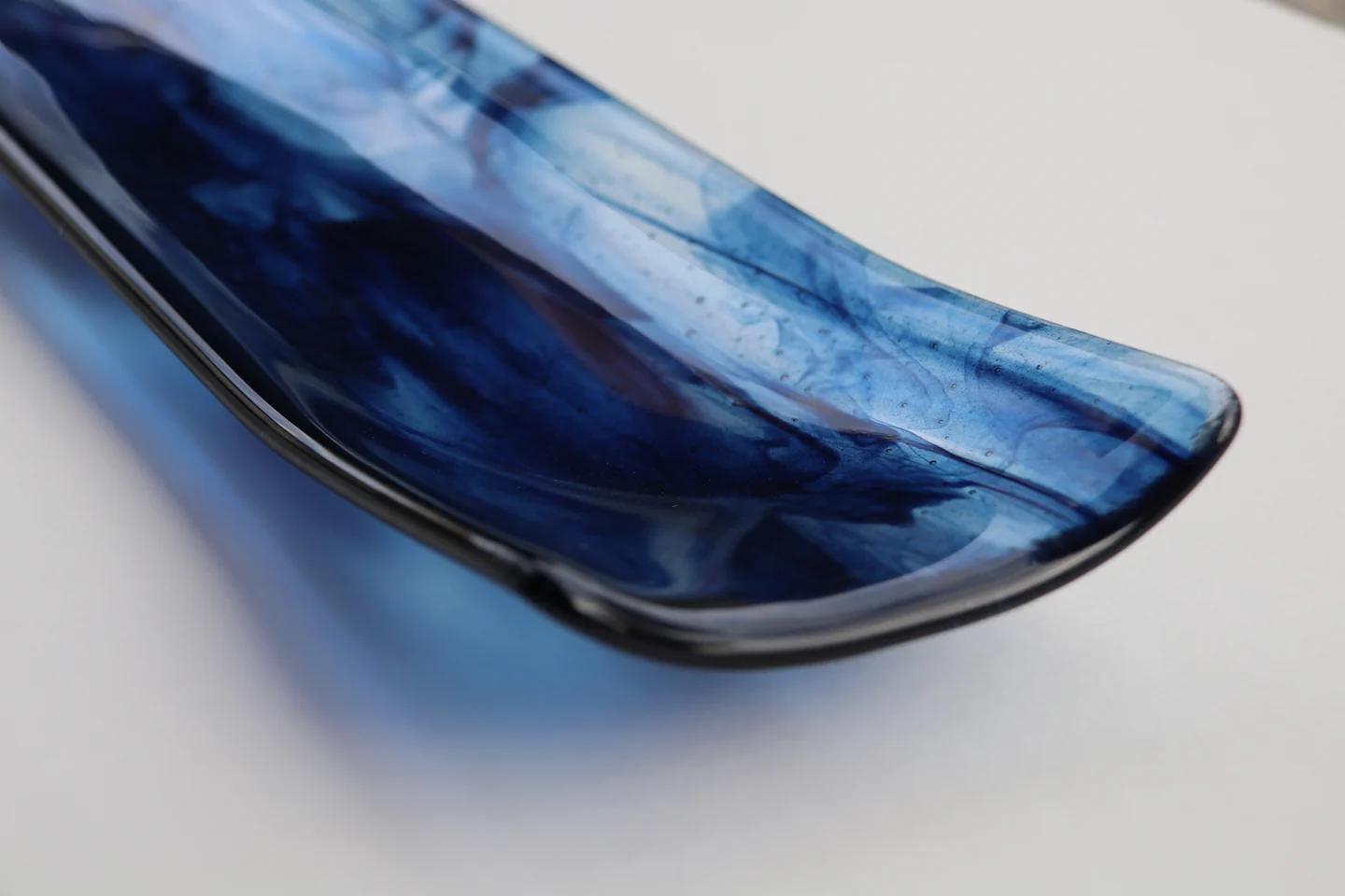 A shallow curved form with dark blue and pale blue streaks is photographed at an angle against white.