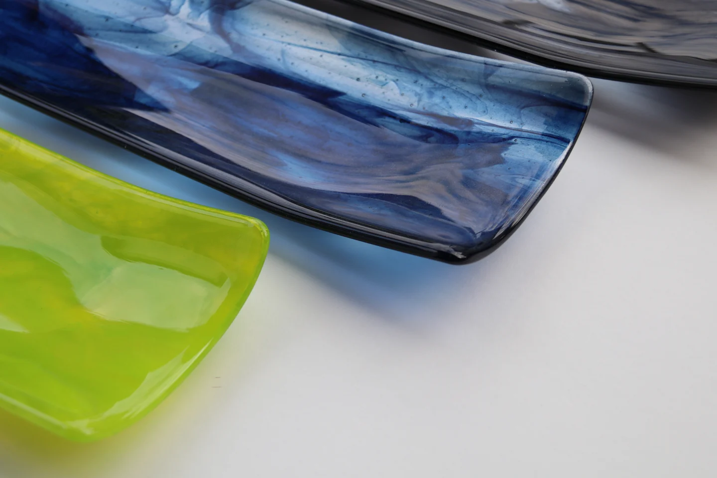 A streaked blue curved form sits behind a partially visible bright green form on a pale surface.