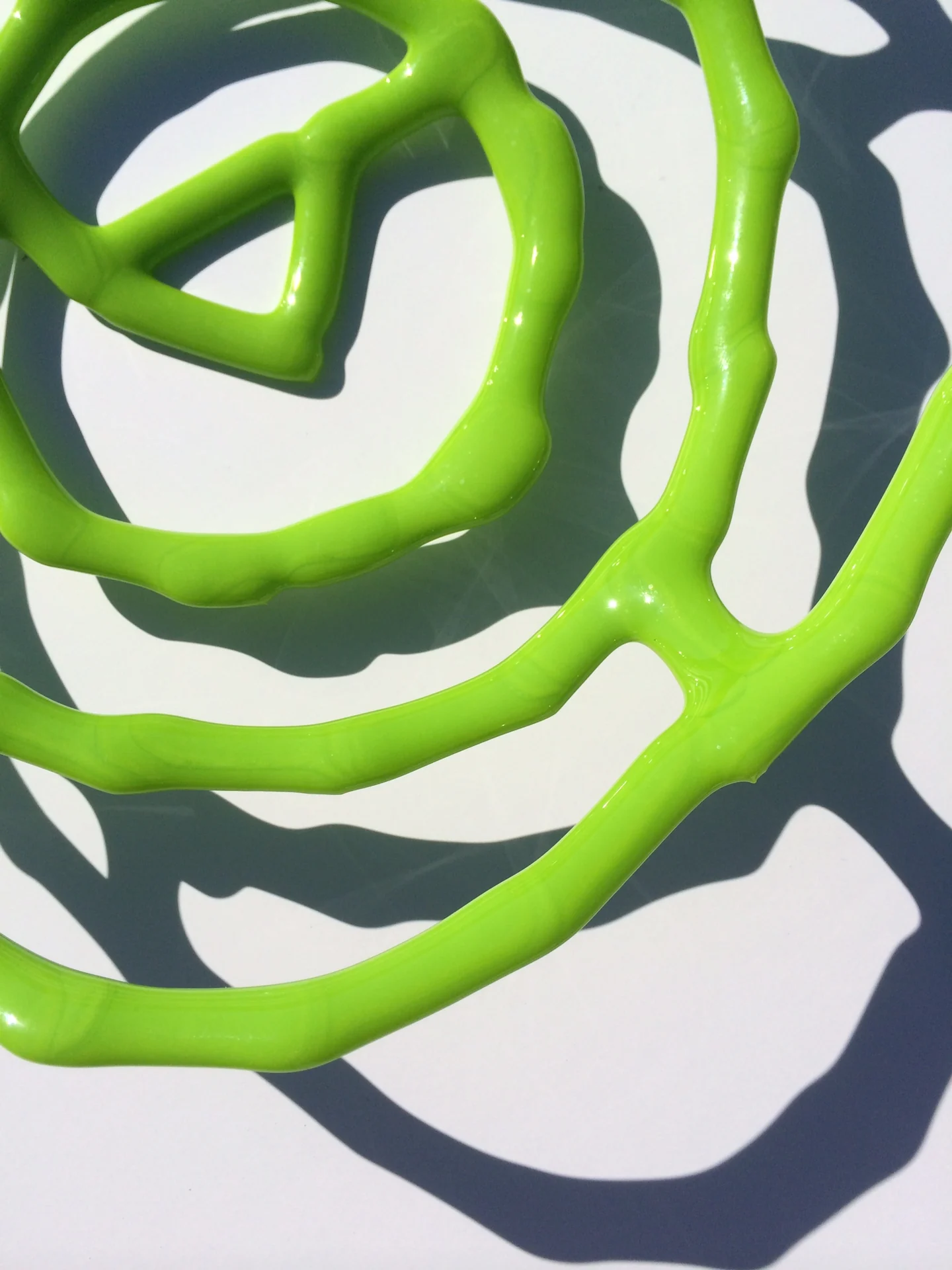 A close overhead view of bright green looping bars shows their dark branching shadows on a light surface.
