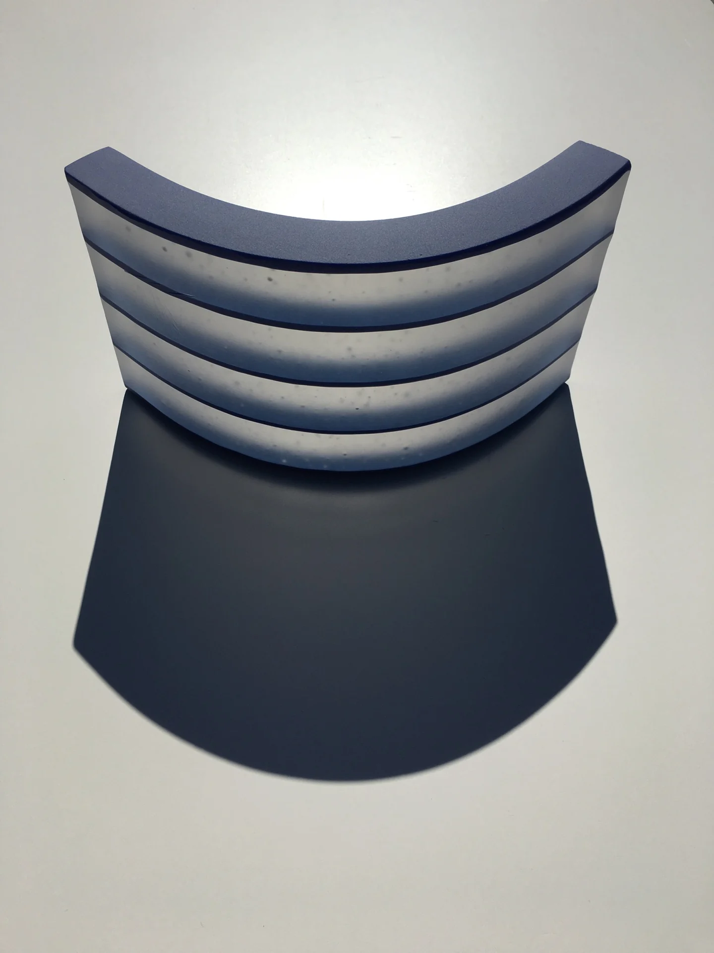 A dark curved form has several pale blue-gray horizontal bands across its upper section against a light background.