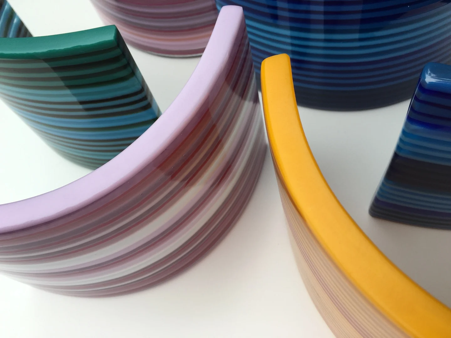 A close view of several curved striped forms shows green, lilac, yellow and two blue sections overlapping on white.