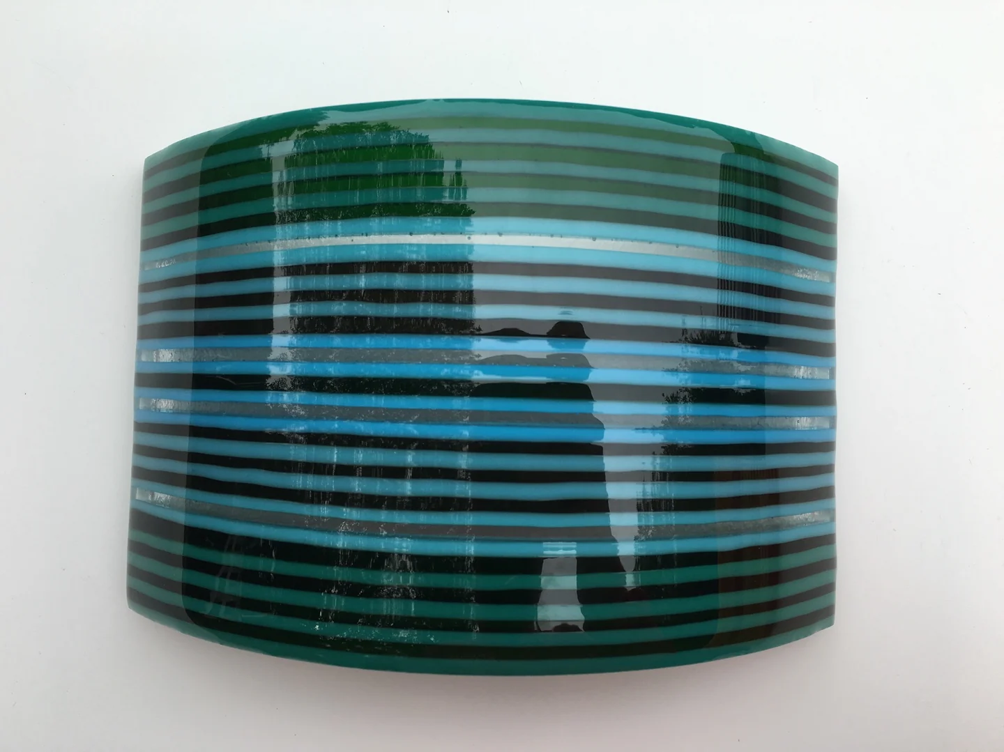 A single broad curved form shows horizontal green, turquoise and dark blue stripes against a pale background.