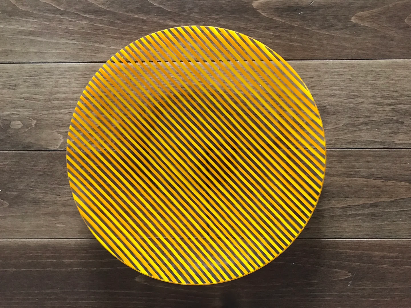 A circular yellow face filled with fine dark diagonal stripes stands against horizontal brown boards.