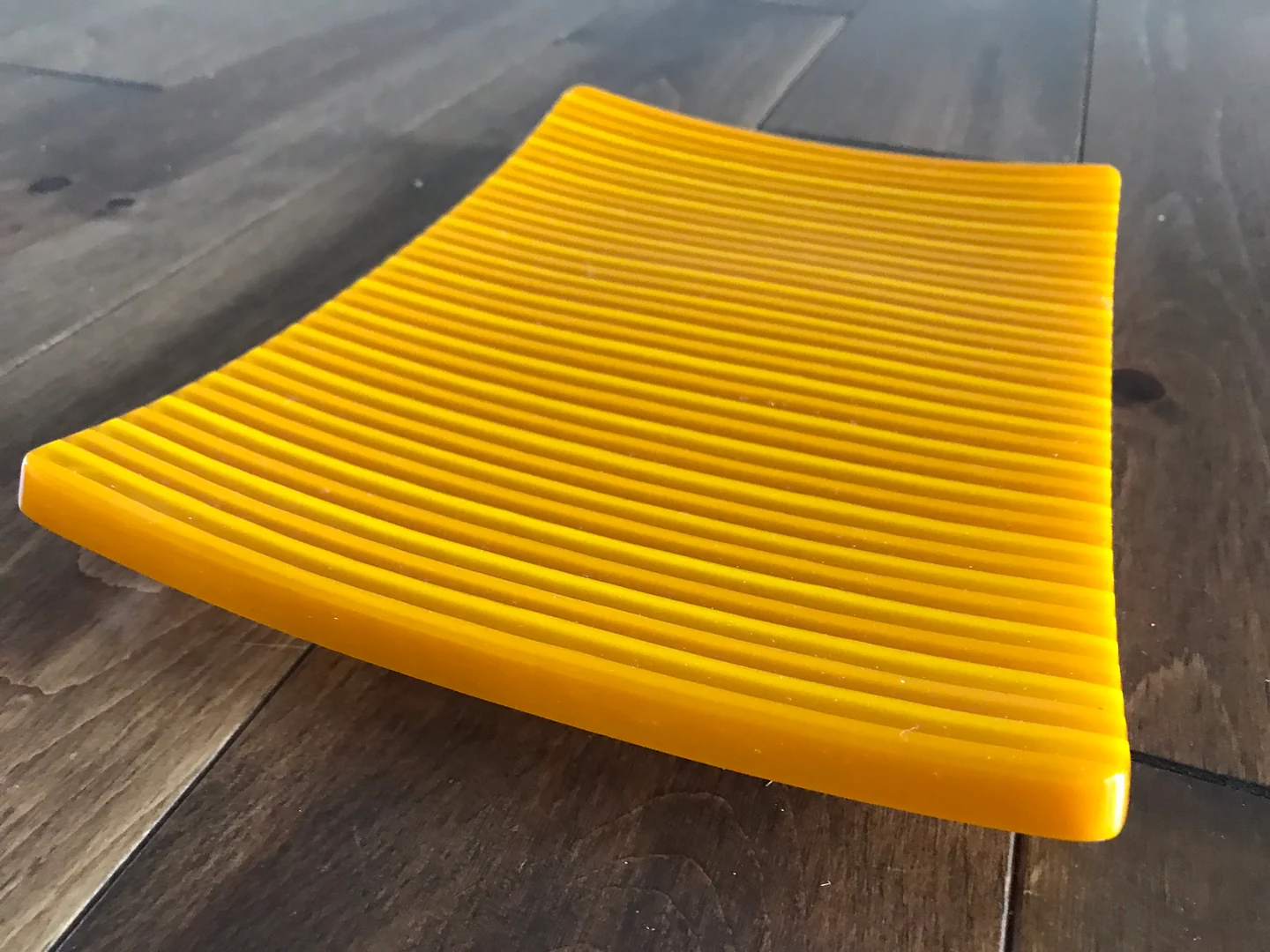 A bright yellow, closely ribbed fan-shaped form rests on a dark wood surface.