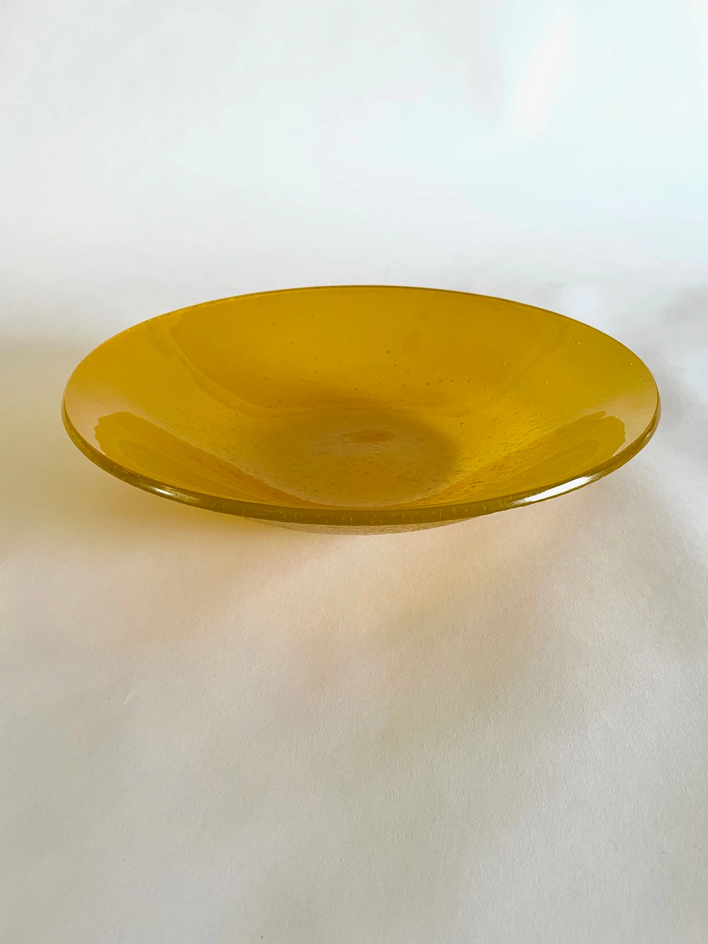 A shallow golden-yellow circular form is shown from above at an angle against a softly lit pale background.