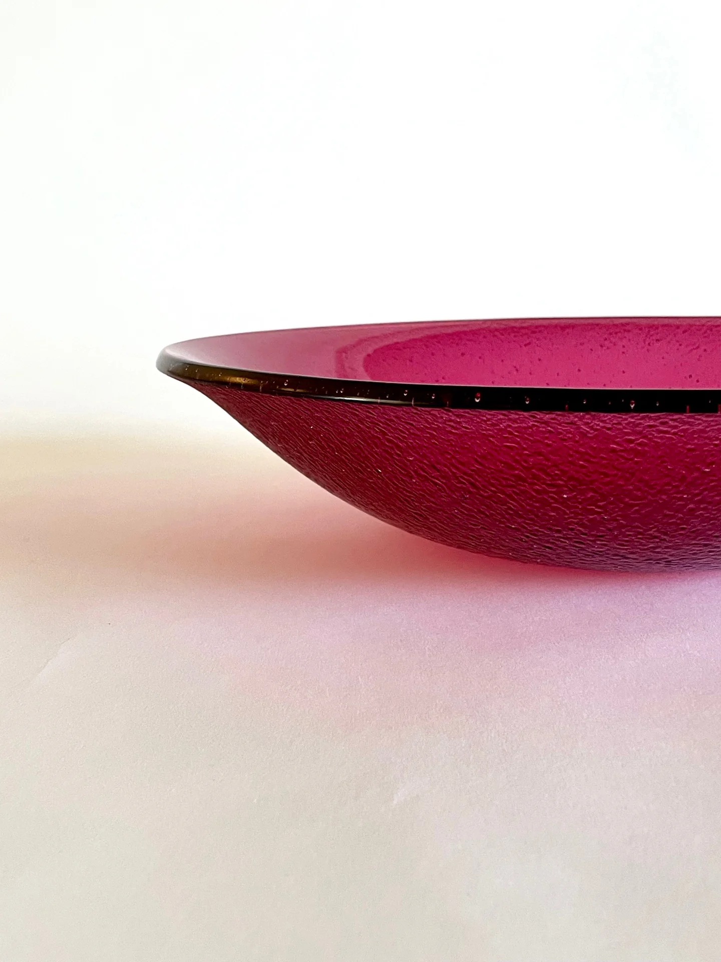 A close side view isolates the pointed rim and curved magenta underside of a shallow form against white.