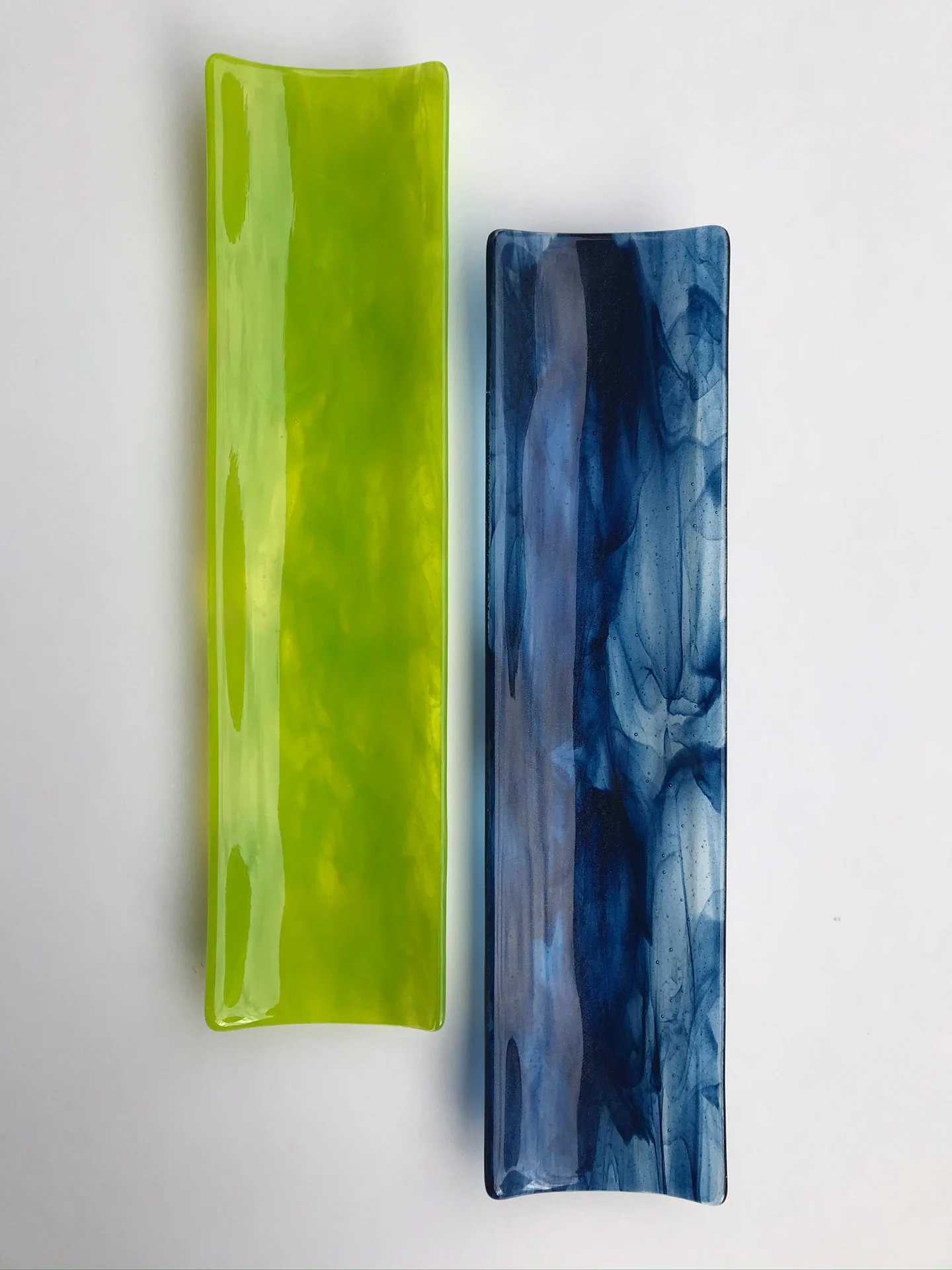 Two long, gently curved rectangular forms, one lime green and one mottled blue, stand side by side against white.