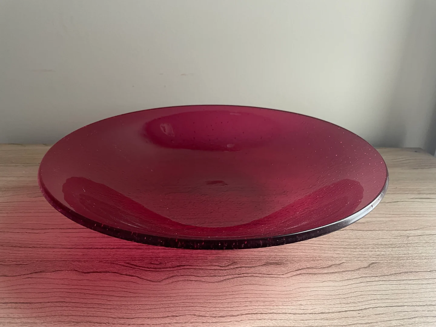 A wide, shallow wine-red bowl with a darker circular center is photographed from above at an angle.