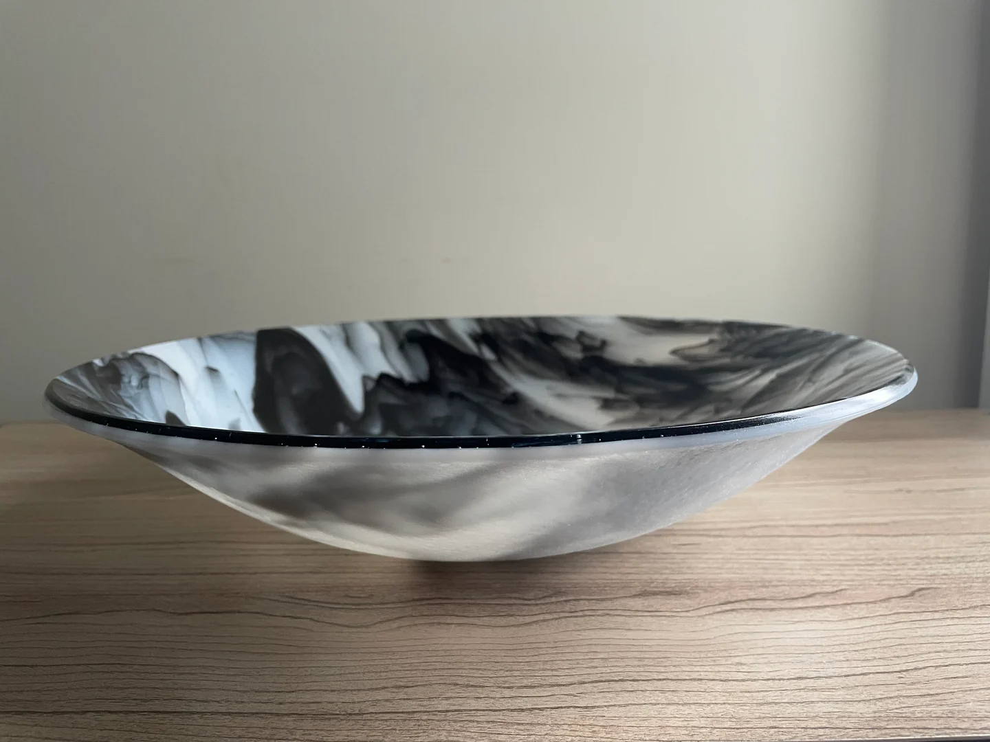 A low side view shows black, white and gray streaks along the wide rim of a shallow bowl.