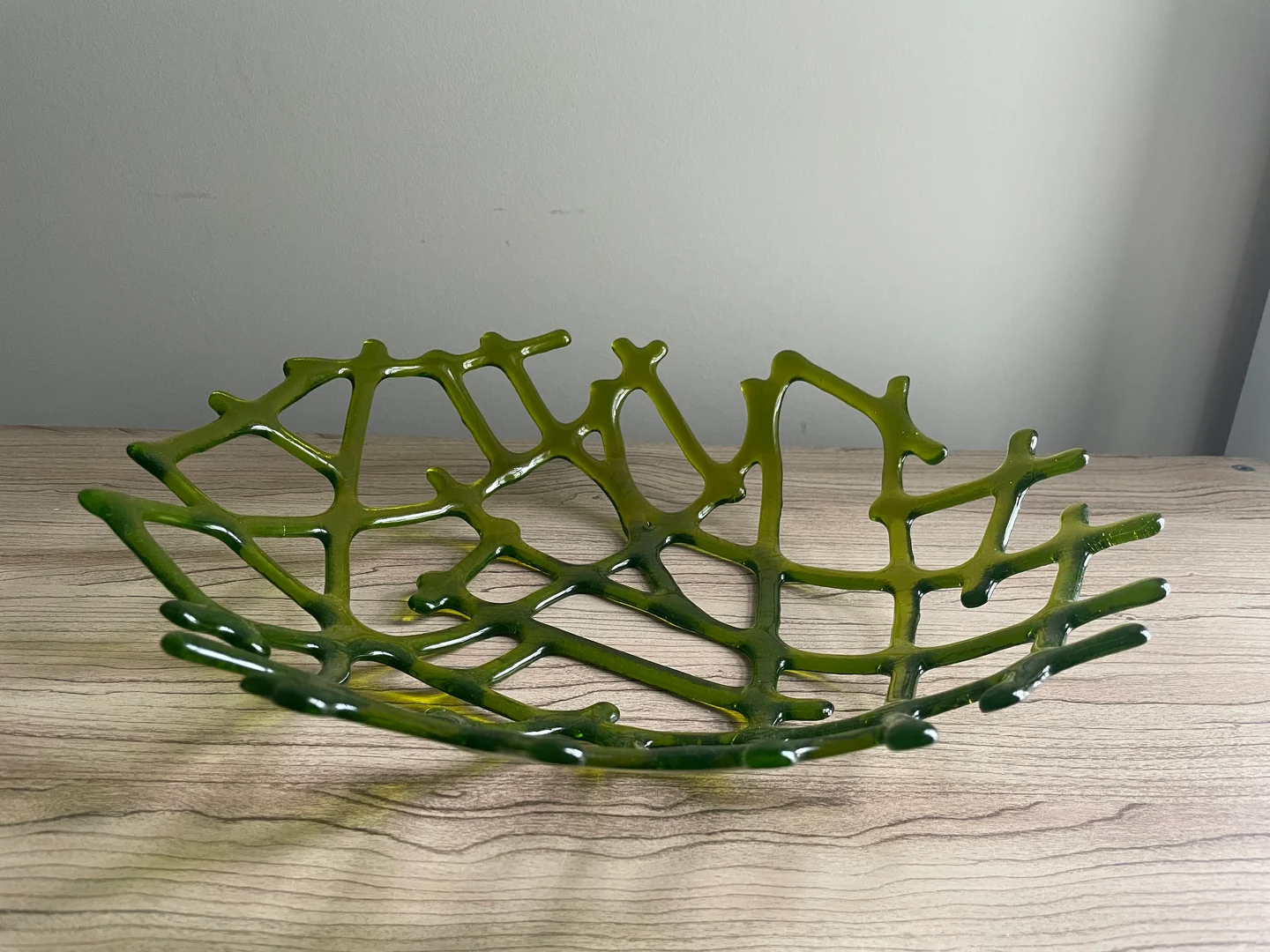 An open, shallow green form is made of irregular intersecting lines and rests on a pale wood surface.