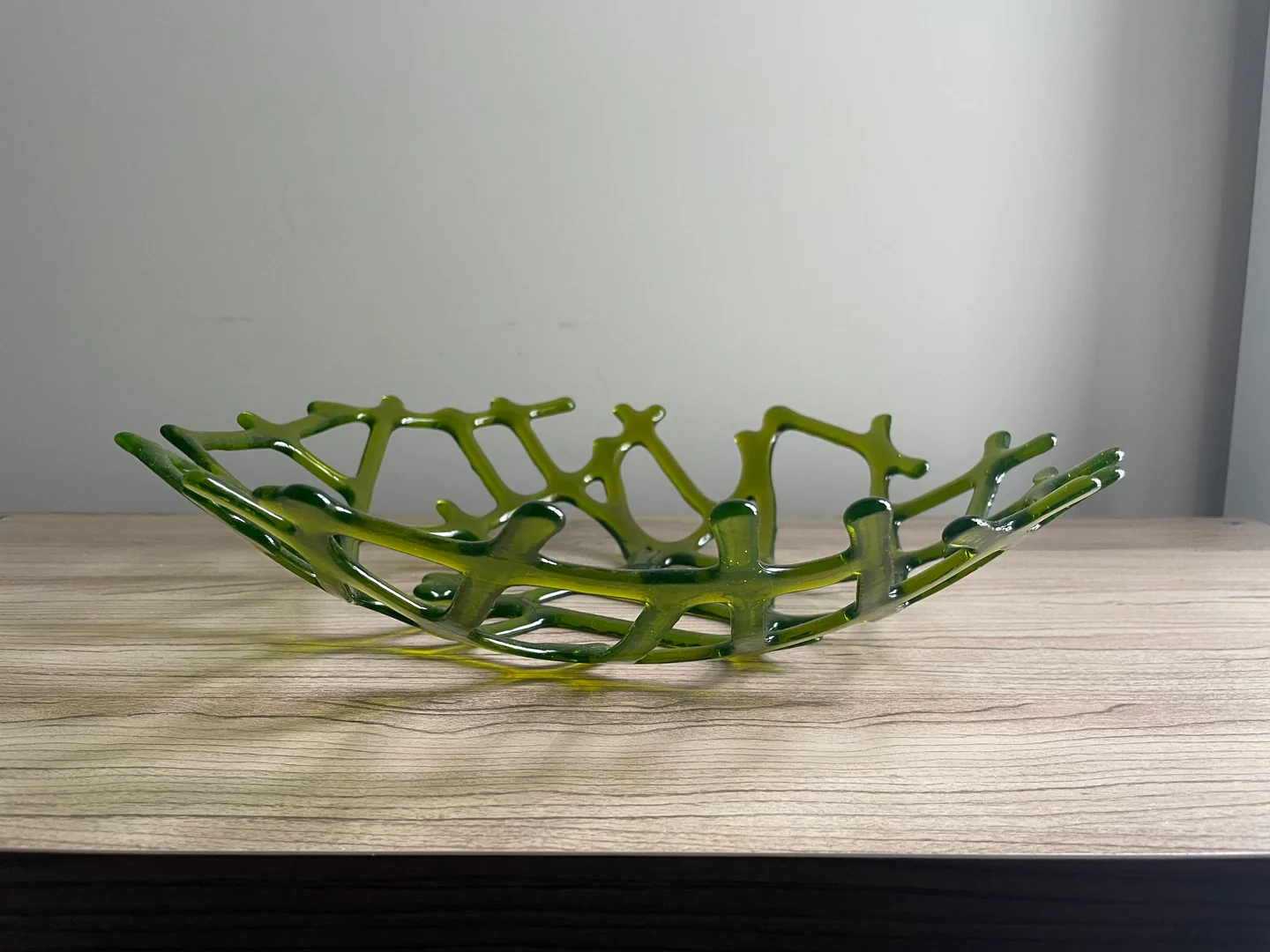 A side view shows the raised, irregular green lattice of an open shallow form on a pale wood surface.