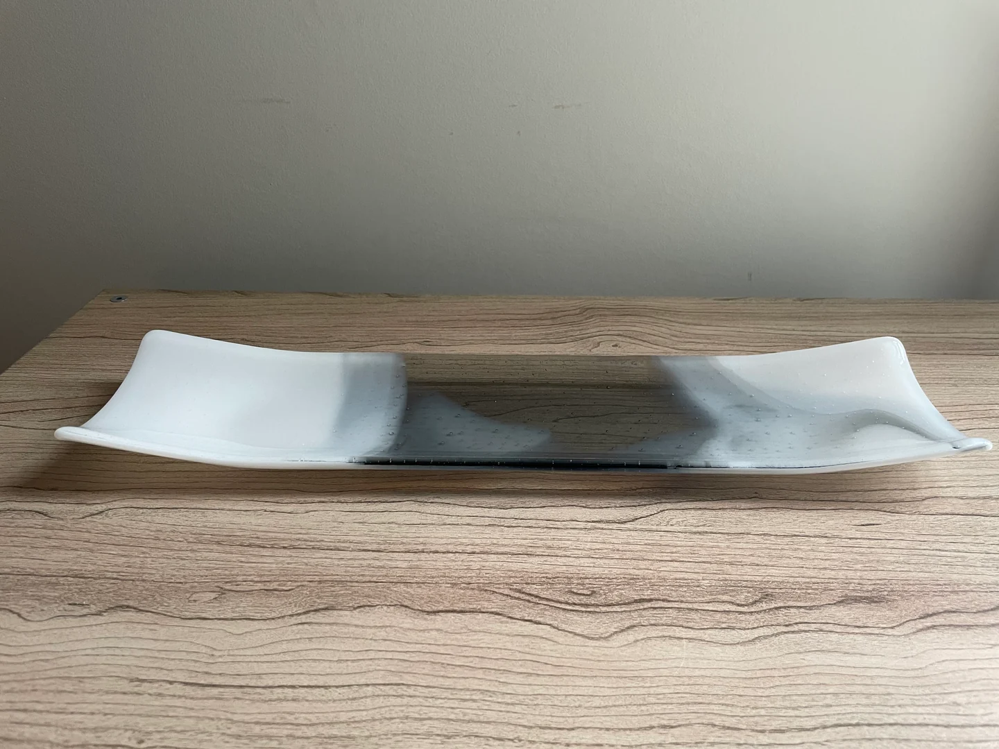 Two long shallow forms lie end to end horizontally on a wood-grain surface, their white ends fading toward gray centers.