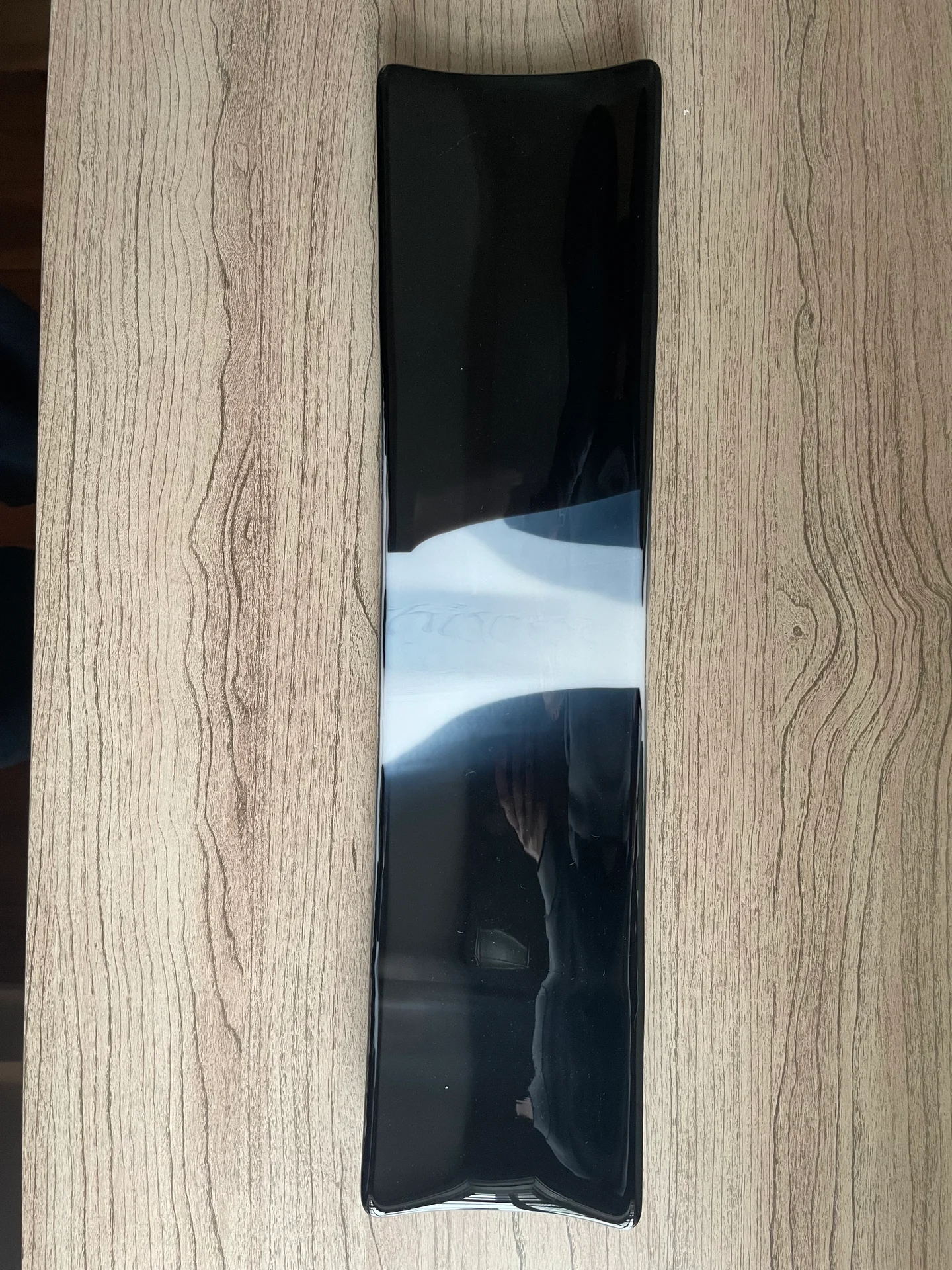 A long, narrow glossy black form with curved ends and a broad white band across its middle lies on a wood-grain surface.
