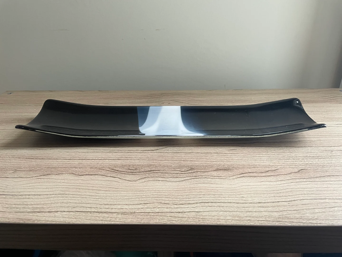 Two long, low black forms with white inner bands face one another across a narrow gap on a wood-grain surface.