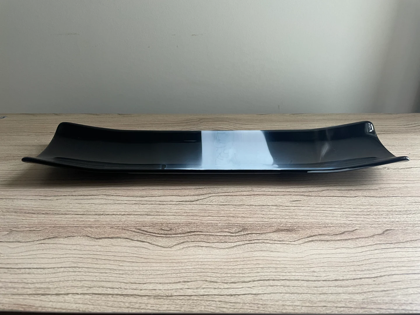 Two low, narrow dark forms with a bright white band between their inner ends lie horizontally on a wood-grain surface.