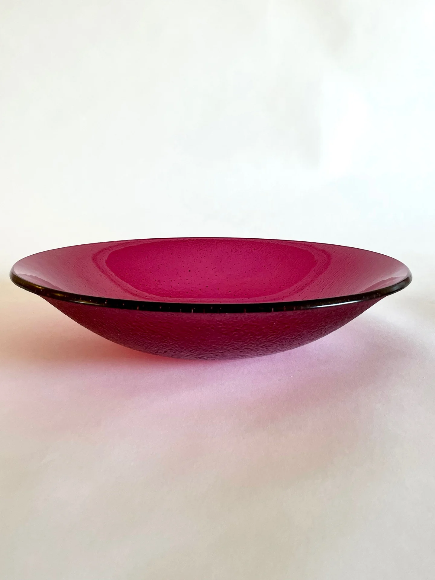 Shallow pink glass bowl photographed on a pale surface