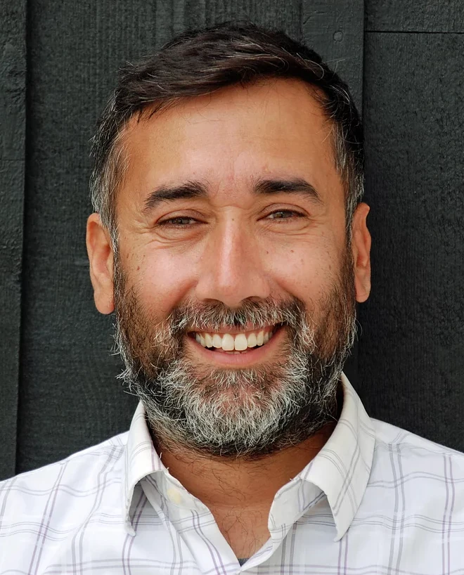 Portrait of Romy Randev smiling in a light shirt against a dark background
