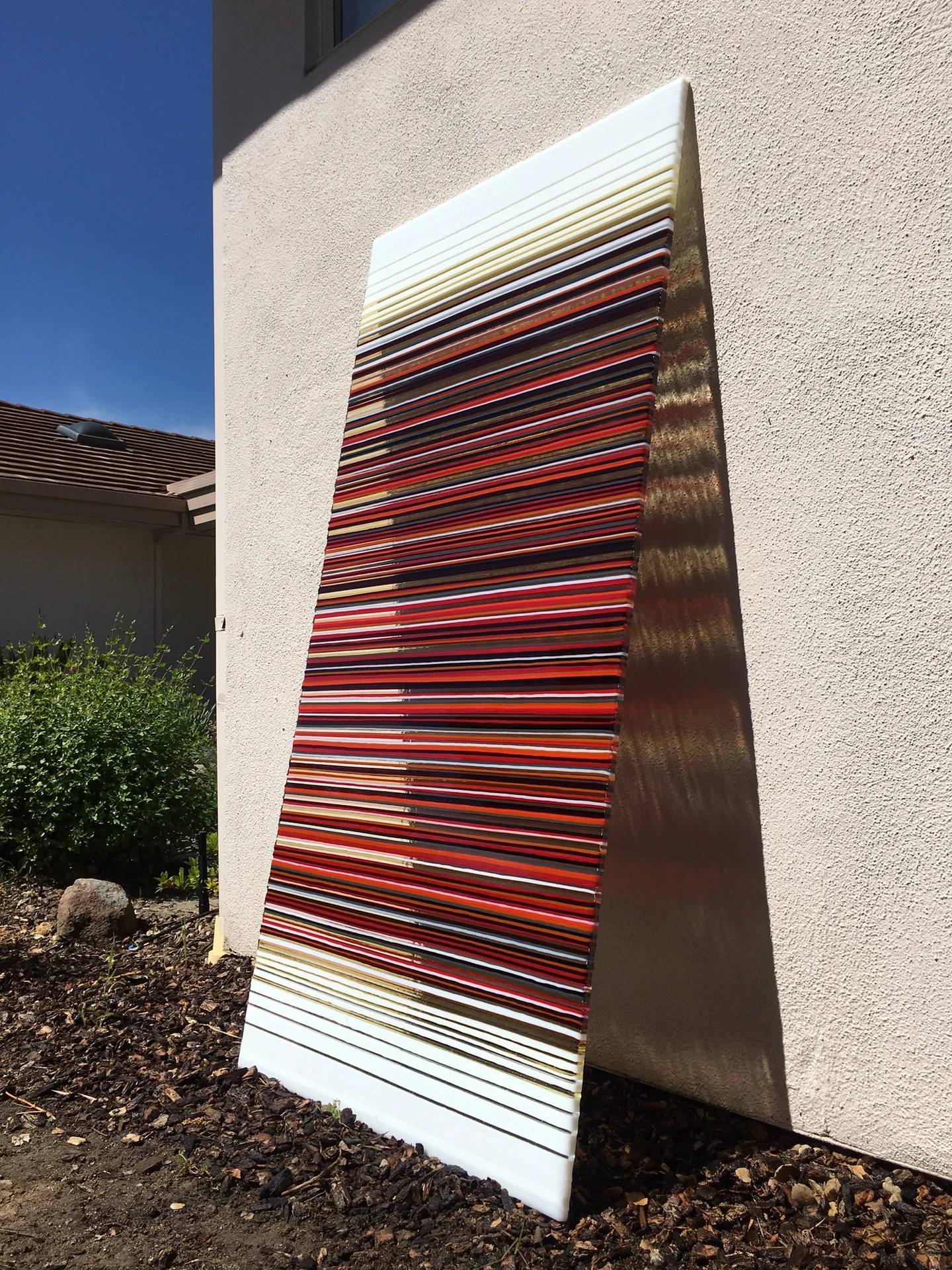 Tall glass panel with dark red and warm-coloured horizontal stripes beside a pale exterior wall